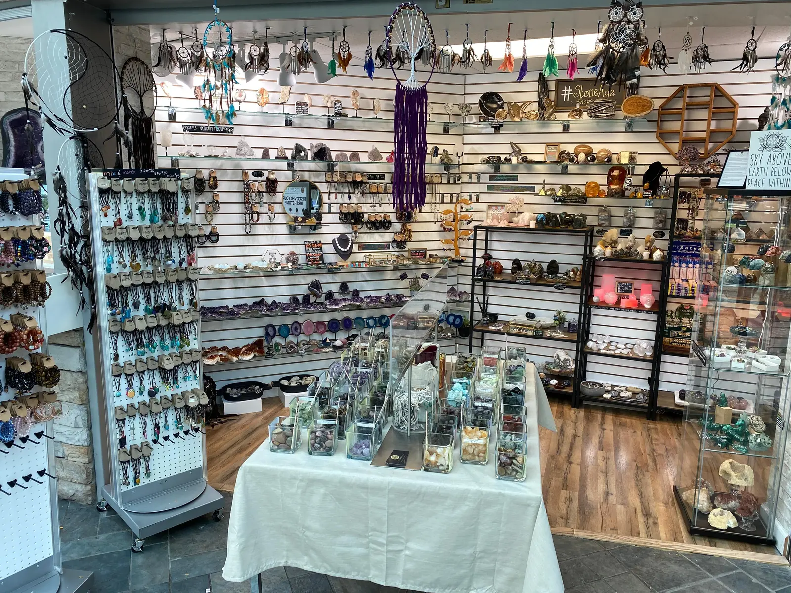 Inside the first Stoneage: a white slatwall packed floor to ceiling with amethyst geodes, agate slices and jewellery, dream catchers hanging from the ceiling rail, and a cloth-covered table of open glass jars of tumbled stones