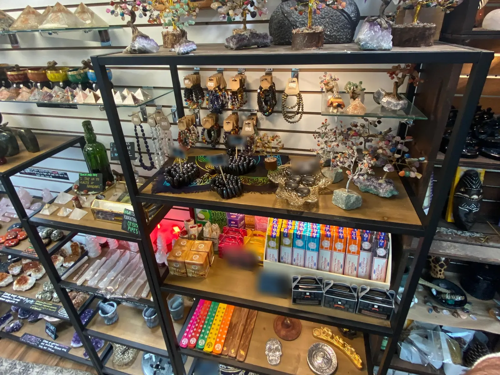 Shelving in the first Stoneage: hematite bracelets on a patterned cloth, gem trees on stands, boxed incense in rows, and carved pieces on the shelf below