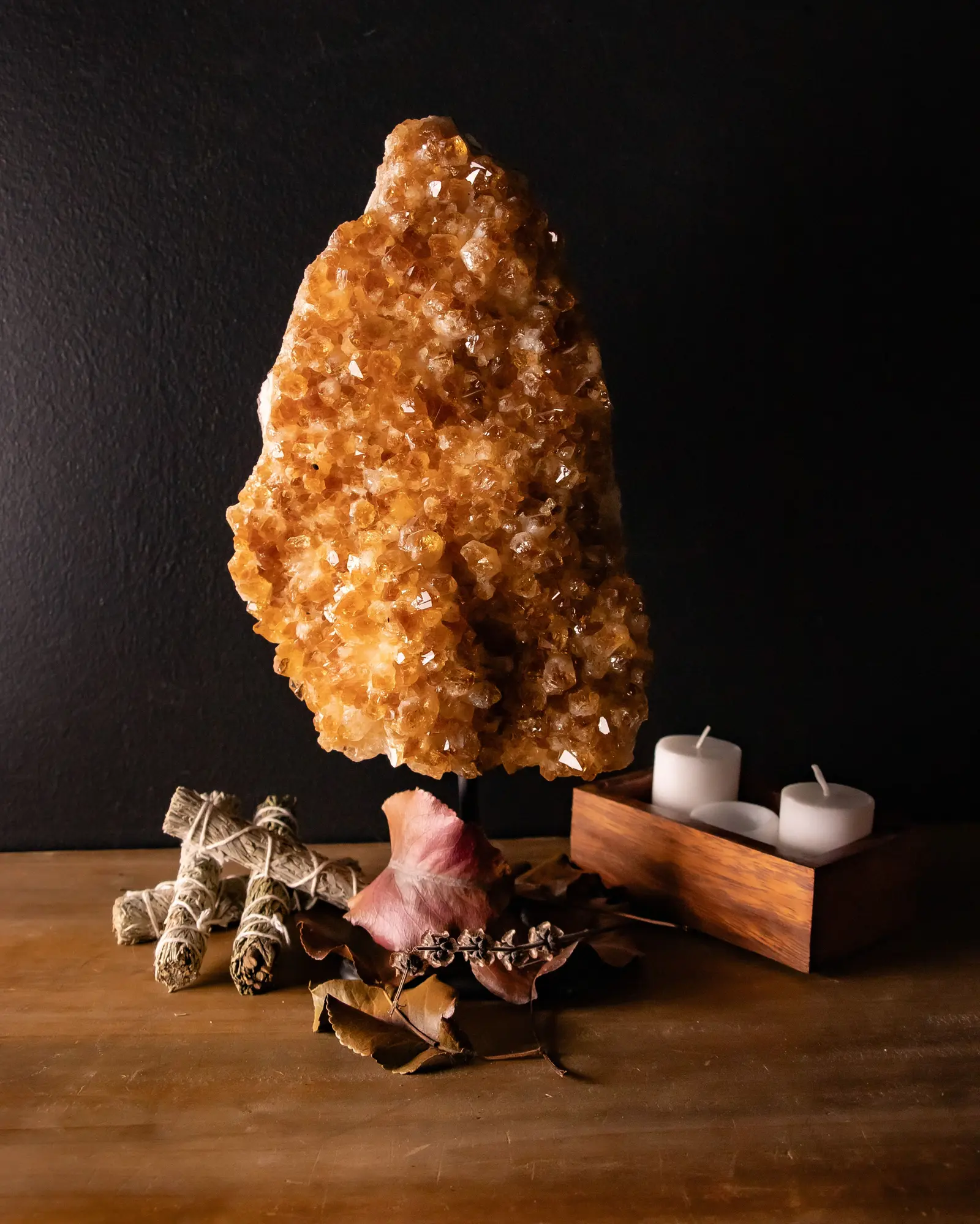 A natural citrine cluster, warm orange points on a pale matrix, standing on a timber shelf beside unlit candles