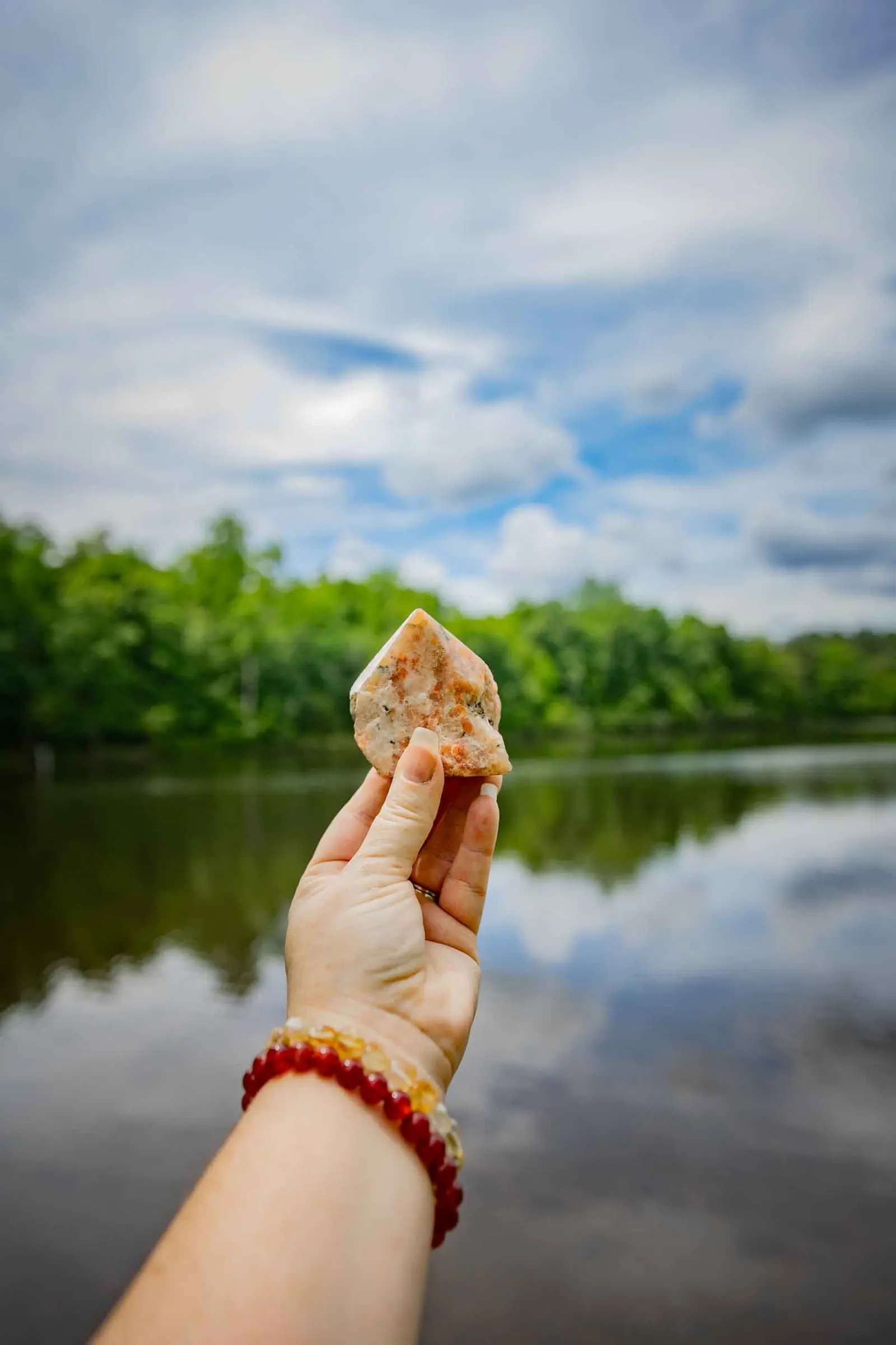A hand holding a raw quartz point against a still lake and open sky