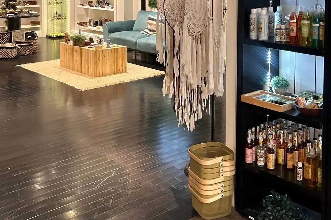 Inside the Town Center at Cobb store: a teal bench under a neon sign reading oh darling you are magic, a macramé rack, open timber shelving of bottles and specimens, and plants along a white wall
