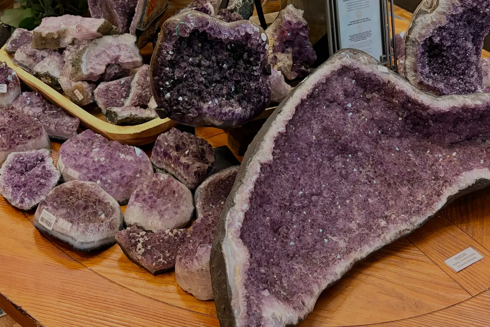 A round timber table stacked with open amethyst geodes at the Jacksonville Mall store, cut faces turned up under warm light
