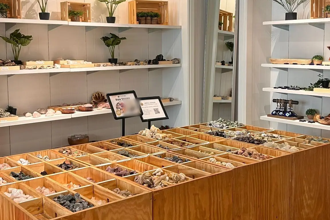 Lit white shelves of raw stones above an open timber bin divided into compartments, each holding a different mineral