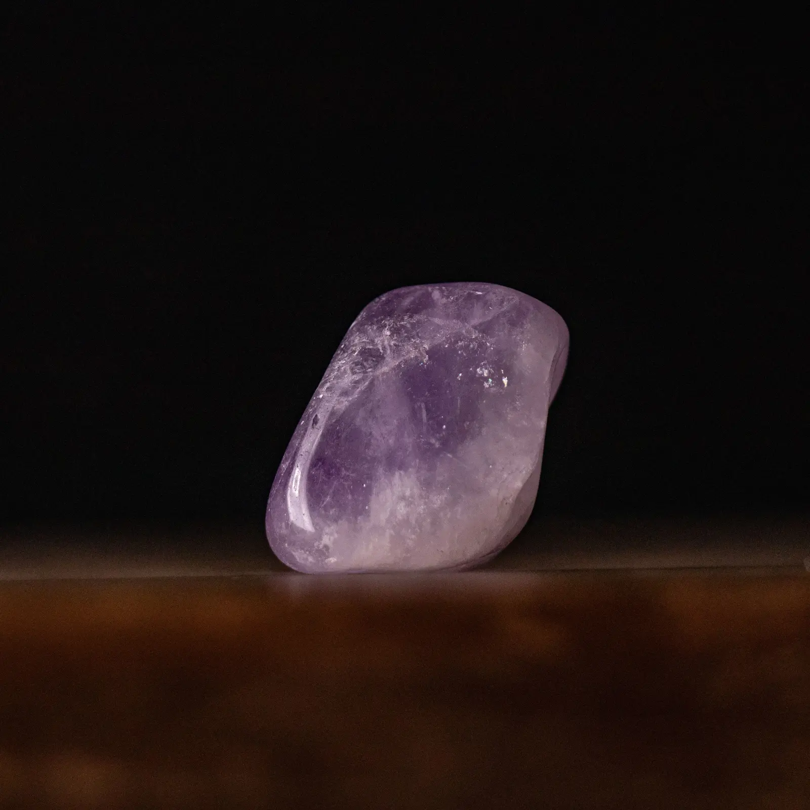 A single polished amethyst on warm timber against black, violet at the top fading to clear at the base