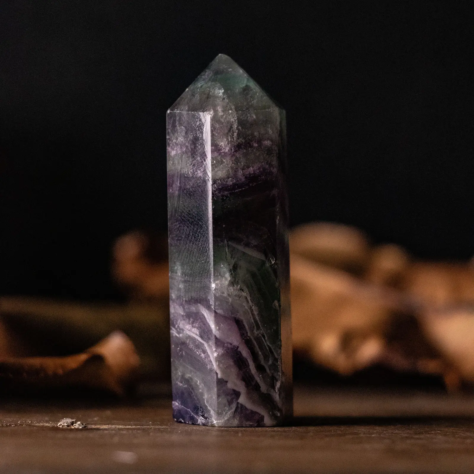 A polished fluorite point standing on timber against black, banded in purple, green and clear