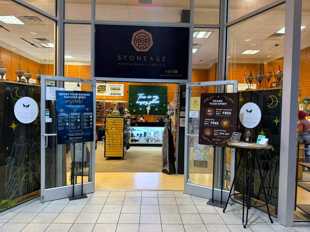 The Cross Creek Mall storefront, gold Stoneage wordmark on black above open glass doors, warm slatted walls and a lit moss wall visible inside